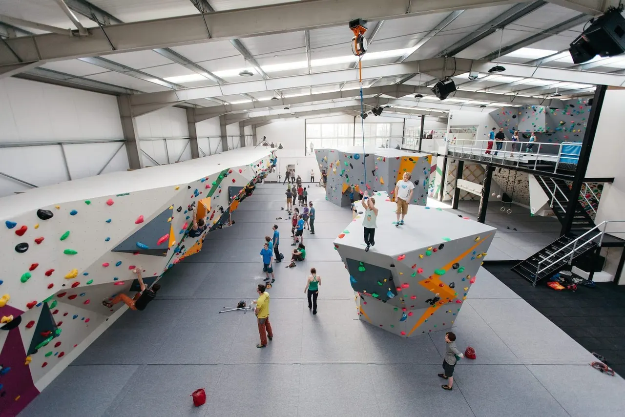 Indoor climbing facility with children and adults climbing coloured holds on multiple large wall structures.