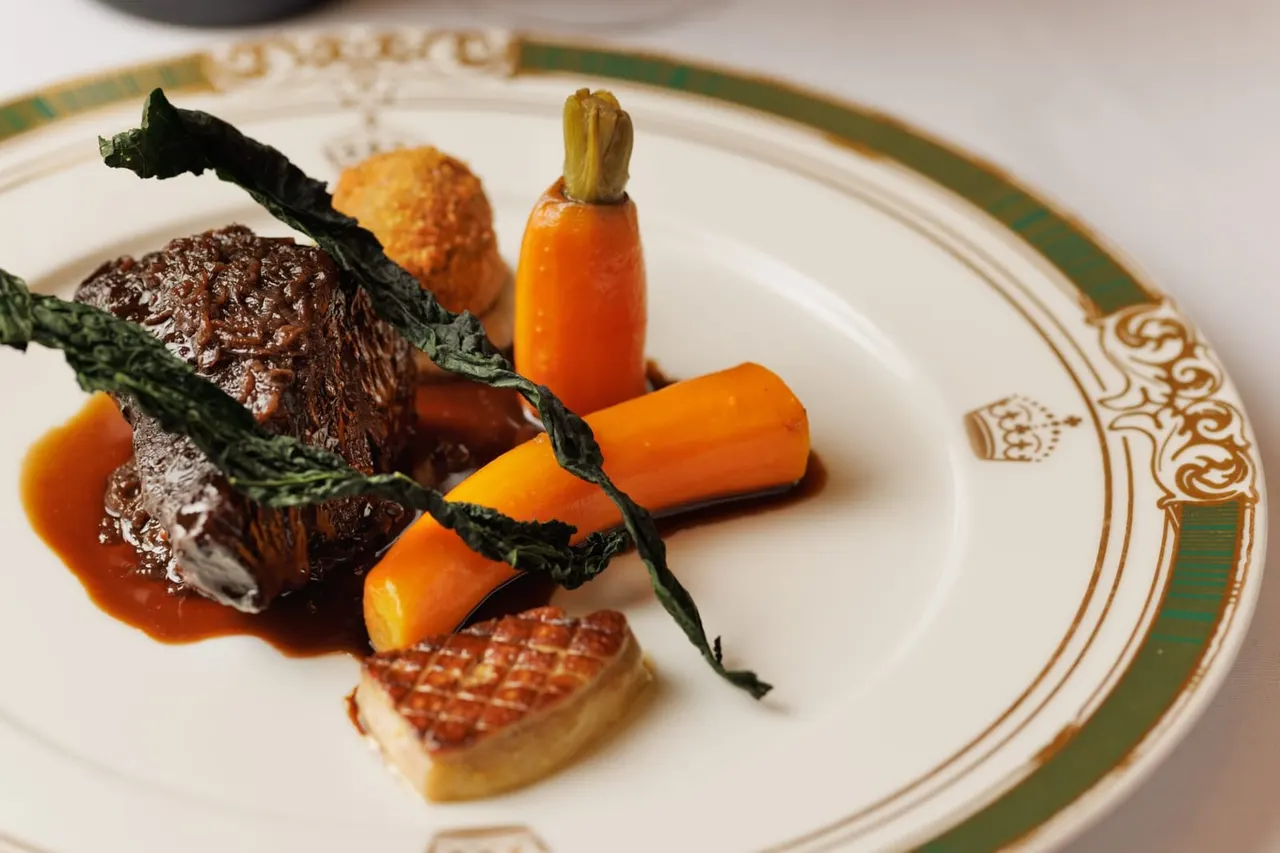 Fine dining plate featuring cooked meat with roasted vegetables, caramelised root vegetables, and garnish on an ornate plate.