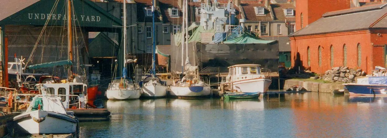 Historic harbour with moored sailing boats and fishing vessels alongside red-brick waterfront buildings.
