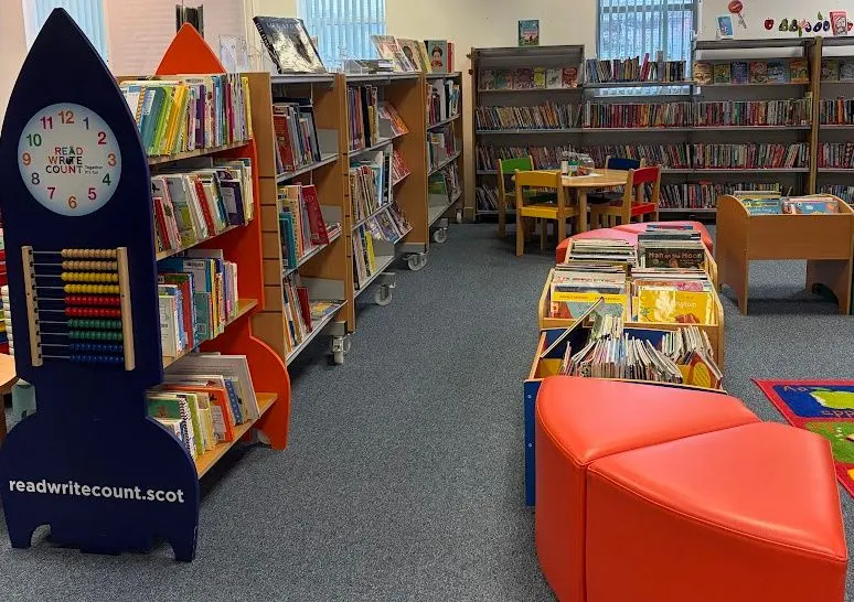 Children's library space with rocket-shaped book storage, colourful seating, shelves of books, and educational displays.