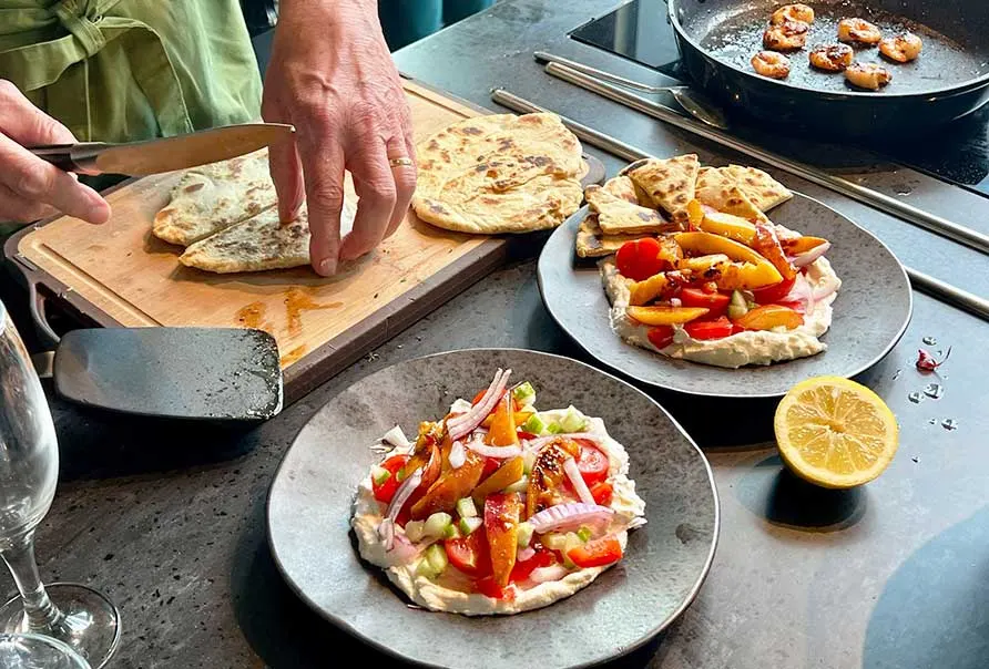 Chef preparing flatbreads topped with roasted vegetables on outdoor cooking counter.