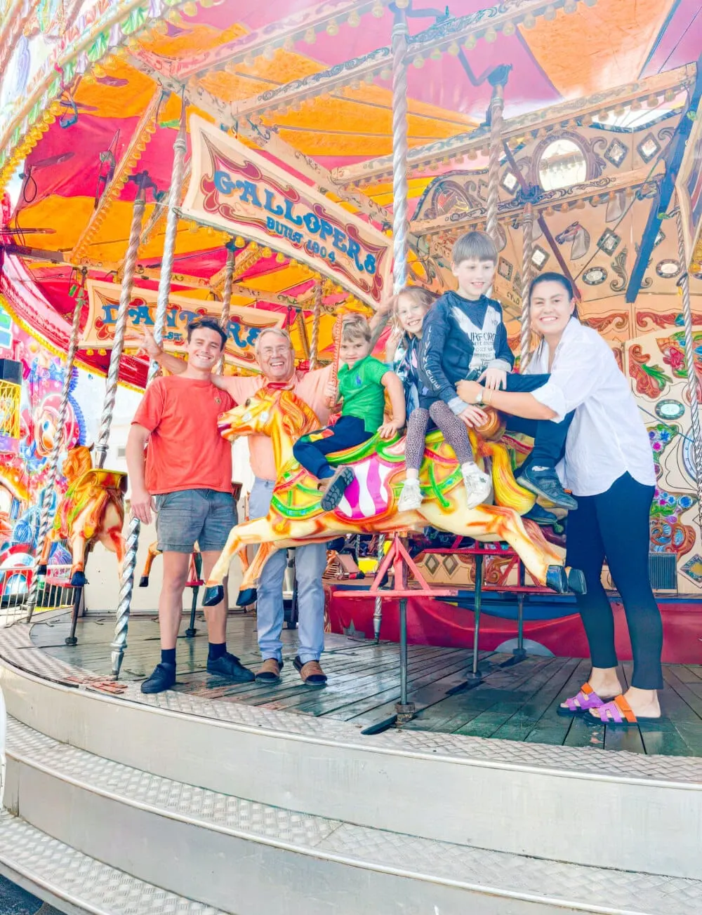 Adults and children posing together on a colourful vintage carousel at a seaside fairground.
