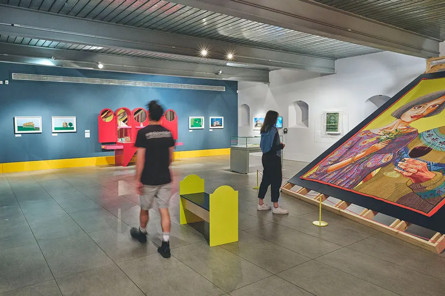 Visitors exploring a contemporary art gallery with blue and white walls, colourful artworks and interactive displays.