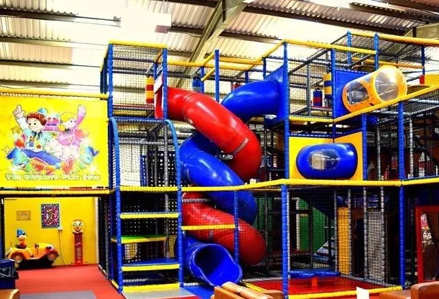 Large colourful indoor play structure with blue and yellow framework, red and blue slides, and tube tunnels in an enclosed facility.