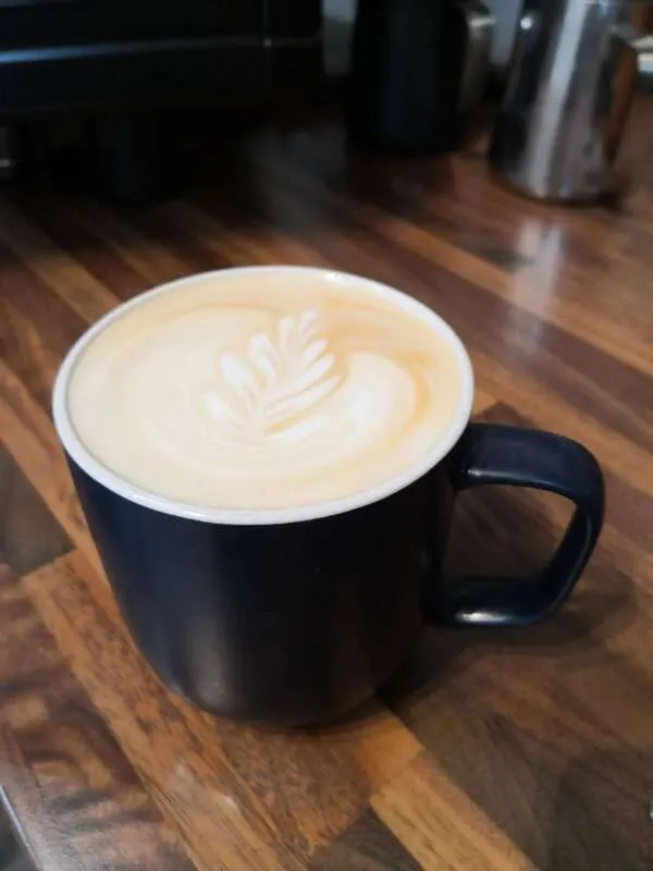 A latte with latte art in a black mug on a wooden café counter.