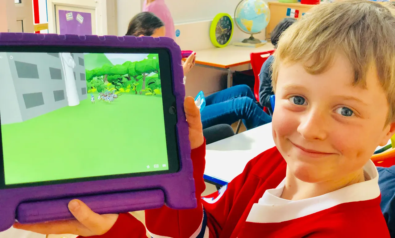 Child holding a purple-cased tablet displaying an animated garden scene in a colourful classroom.