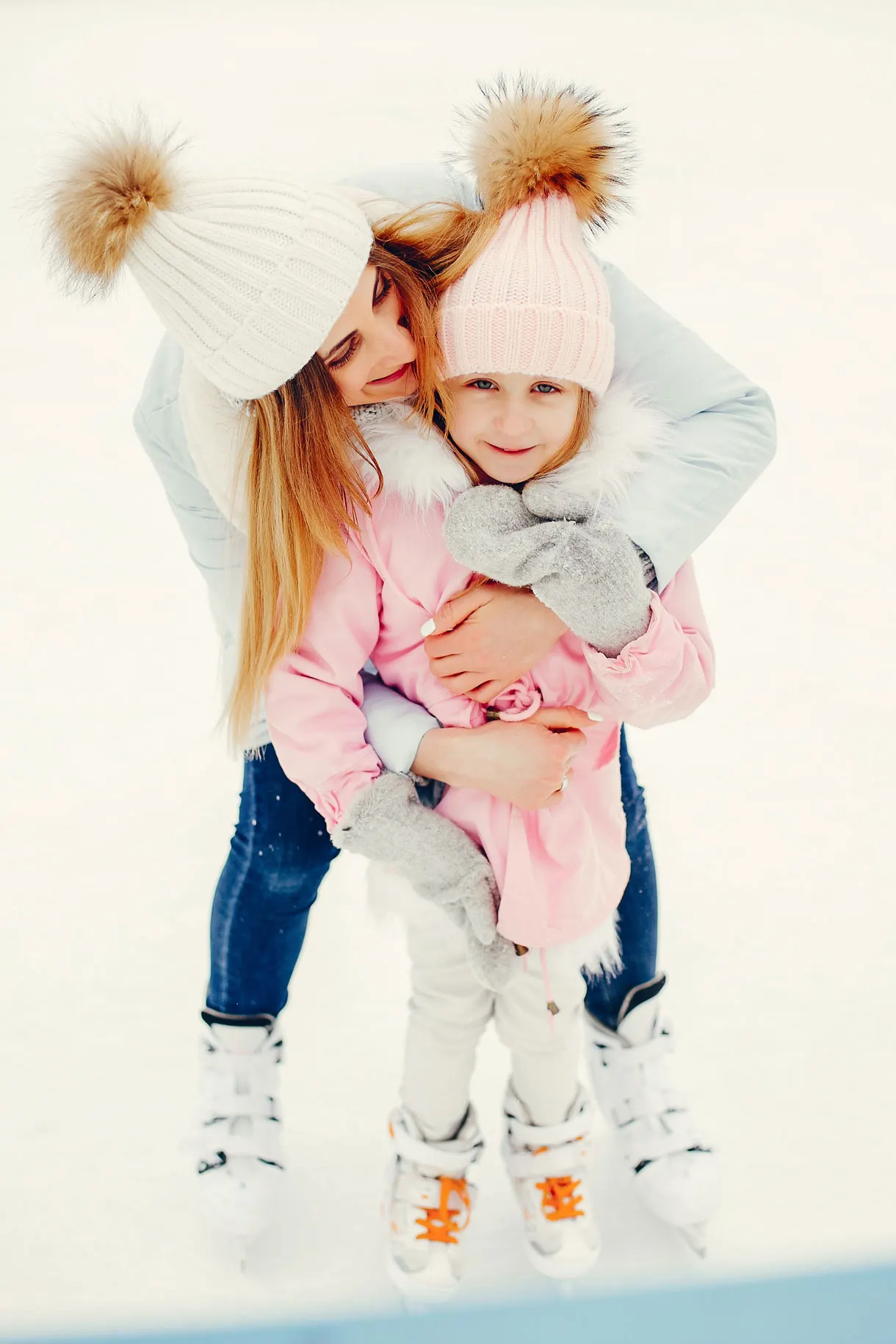 Two young girls in winter clothing playing together in snow.