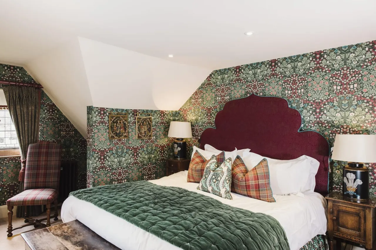 Luxurious bedroom with burgundy velvet headboard, green quilted bedspread, tartan cushions, and floral wallpaper in a period-style hotel room.