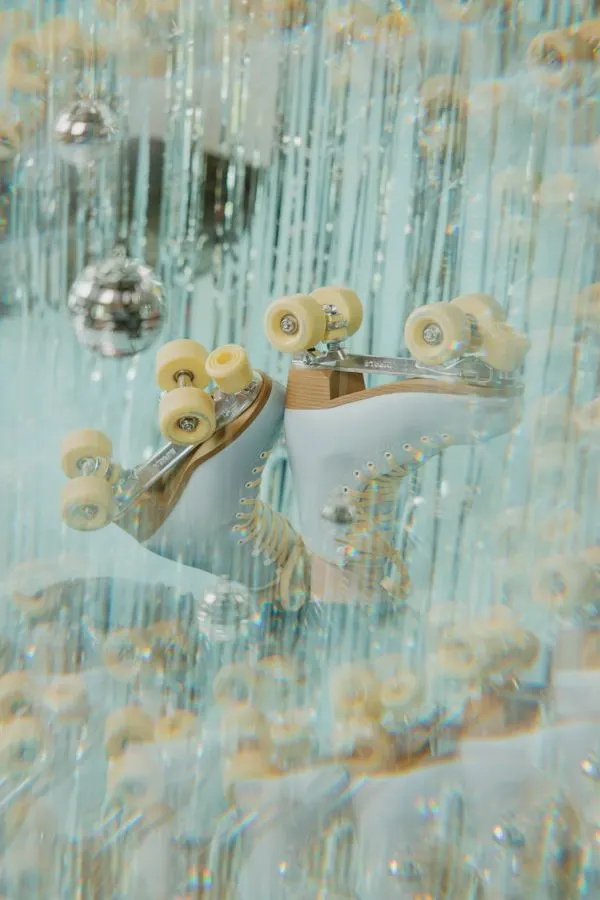Pair of roller skates with cream wheels and metal fixtures against a shimmering turquoise and gold textured backdrop with hanging disco balls.