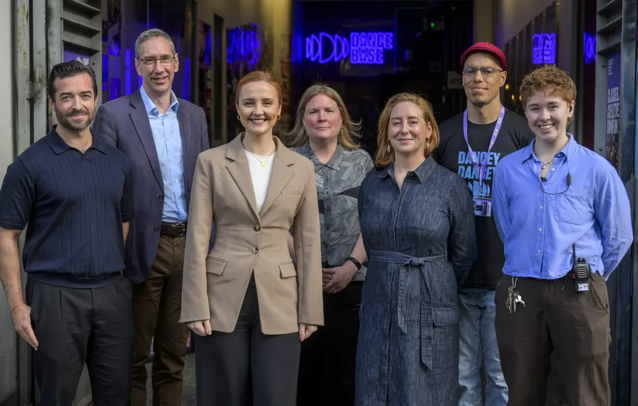 Seven staff members standing together indoors at a dance venue with blue neon signage visible behind them.
