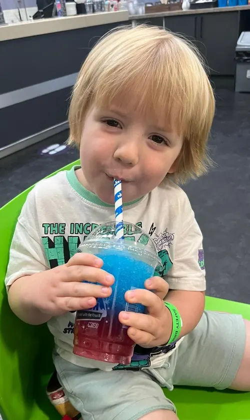 Young child with blonde hair holding a blue drink with a straw at an indoor trampoline park.