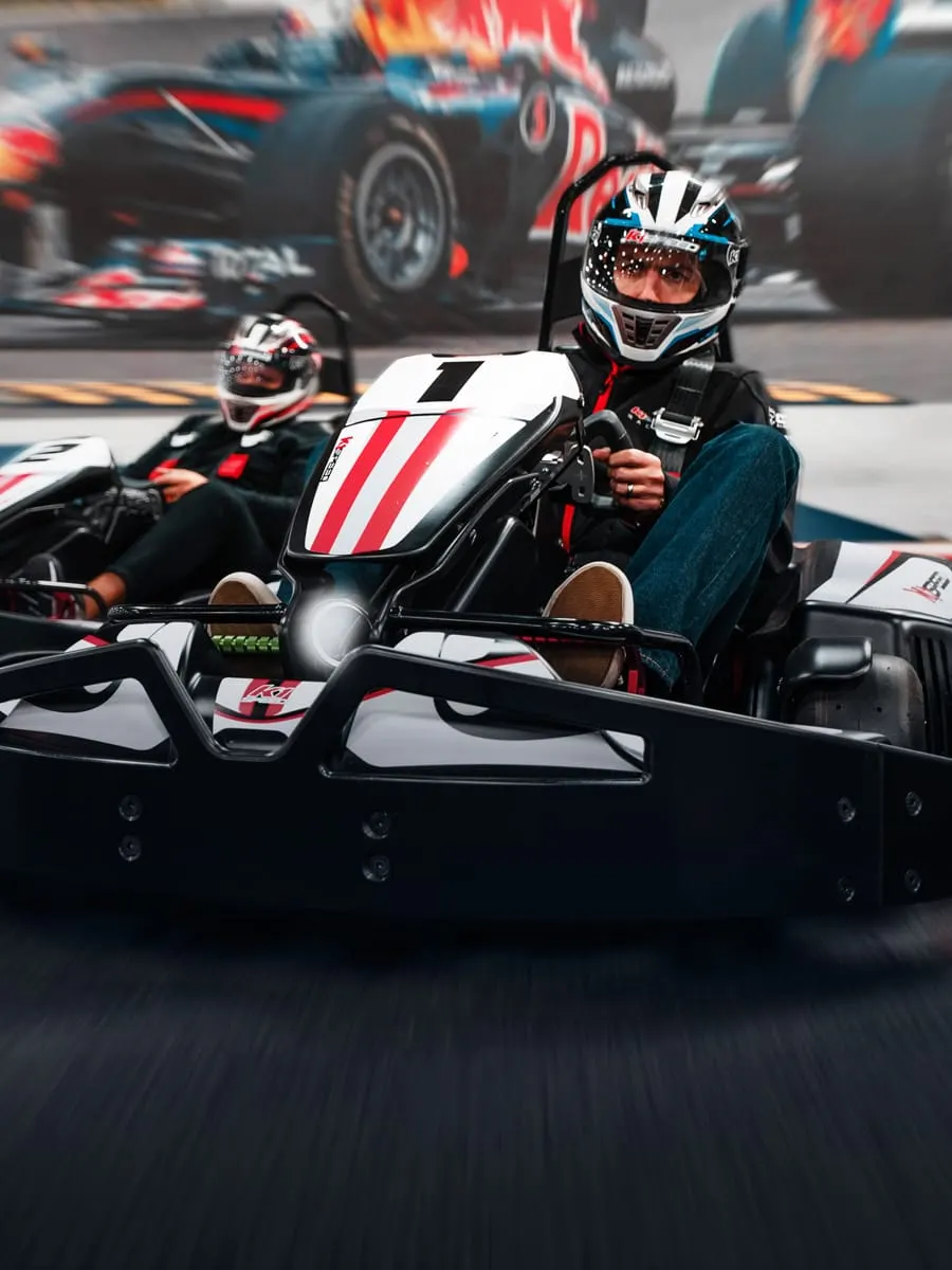Person in helmet and safety gear driving a red and white go-kart on a track with other karts blurred in background.