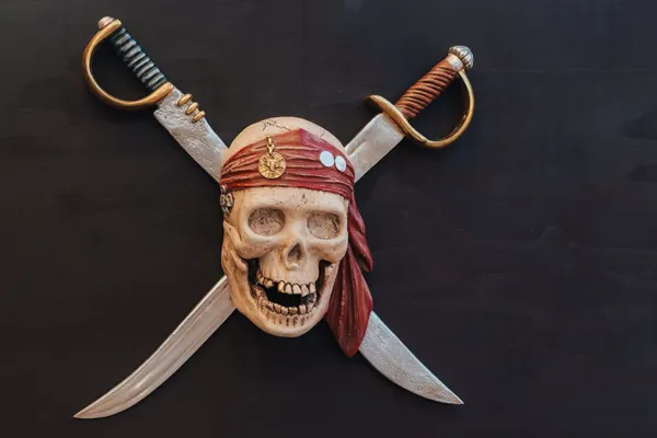 Pirate skull with crossed swords and gold-handled hilts mounted on dark background.