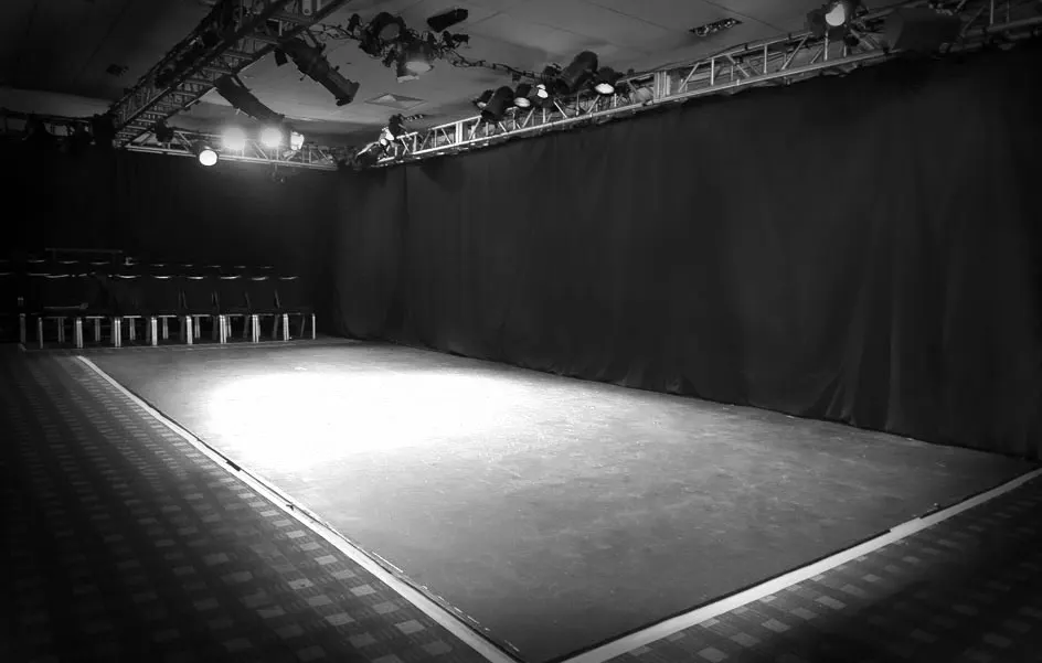 Empty performance stage with professional lighting rig and seating area in black and white.