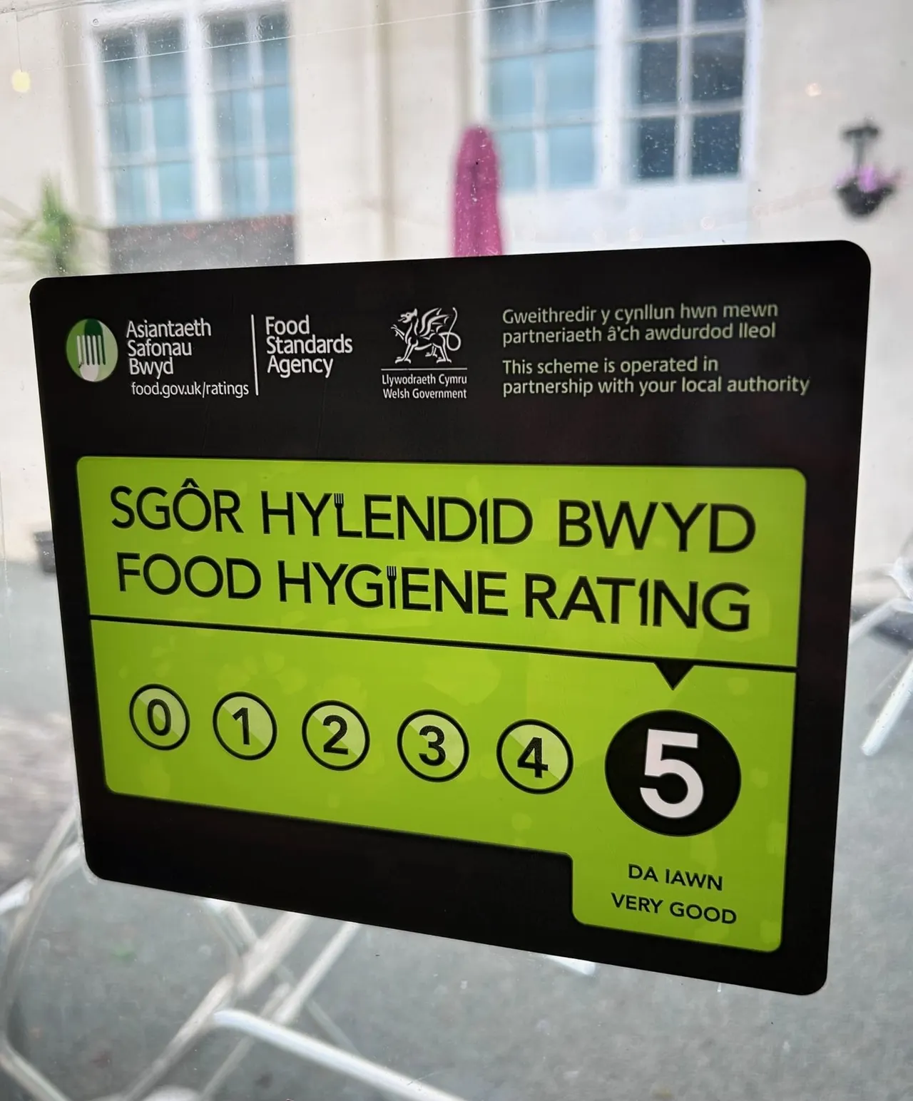 A Food Standards Agency food hygiene rating sticker displaying a 5-star rating displayed in a window of a stone building.