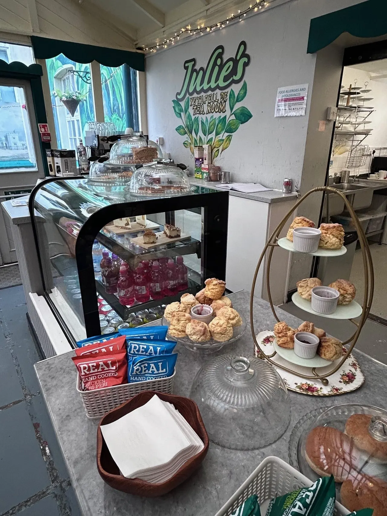 Interior of a tea room counter displaying cakes, scones and baked goods in glass cases and tiered stands.