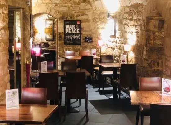 Stone-walled interior of a theatre bar or café with wooden tables, black chairs, and atmospheric lighting.