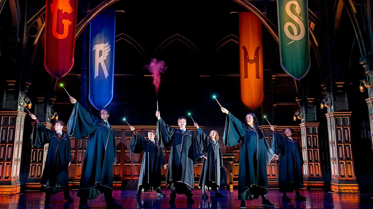 Performers in wizard robes cast spells with illuminated wands beneath floating banners in a magical themed theatre show.