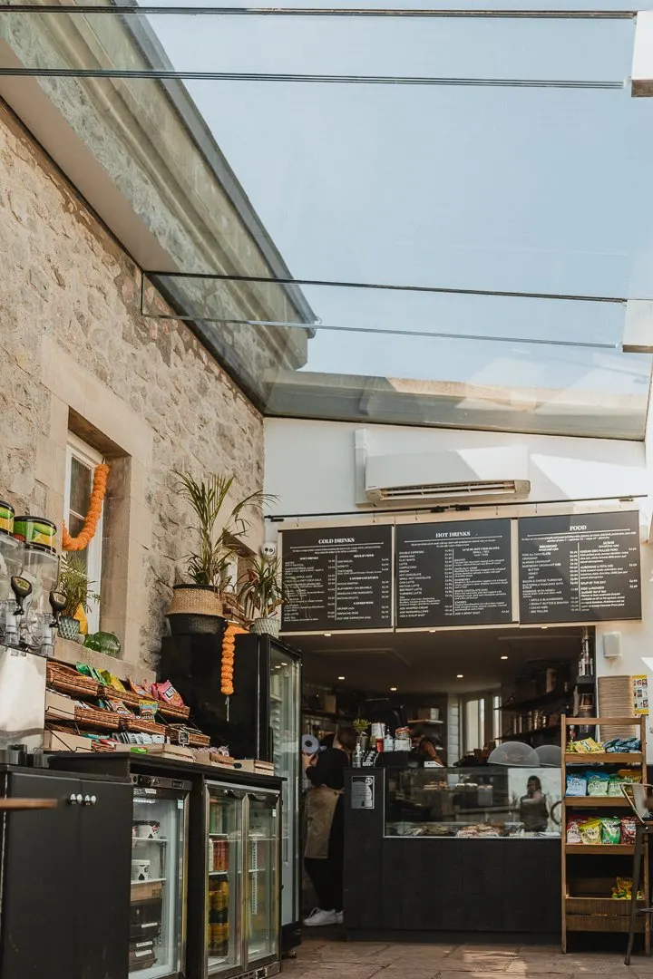A café or food counter built into a stone building with a glass roof, displaying menus and serving customers inside.