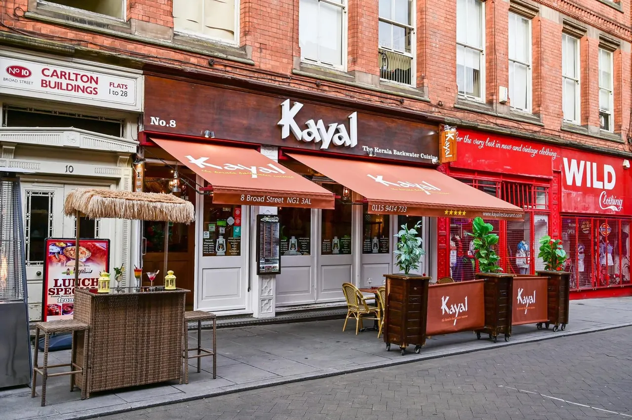 PHOTOGRAPH

Front exterior of Kayal restaurant on Broad Street showing red awning, white entrance doors, outdoor seating area, and potted plants on the pavement.