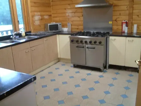 Kitchen with cream and wood cabinetry, professional range cooker, and blue-patterned flooring in a log cabin.