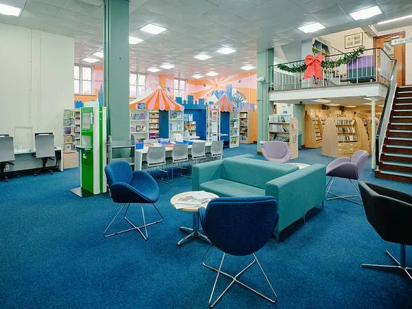 Bright, modern children's library space with turquoise seating, bookshelves, and a striped tent-like structure.