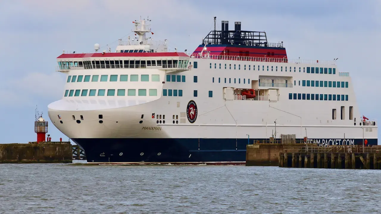 Large passenger ferry docked at a pier, viewed from the water on a clear day.