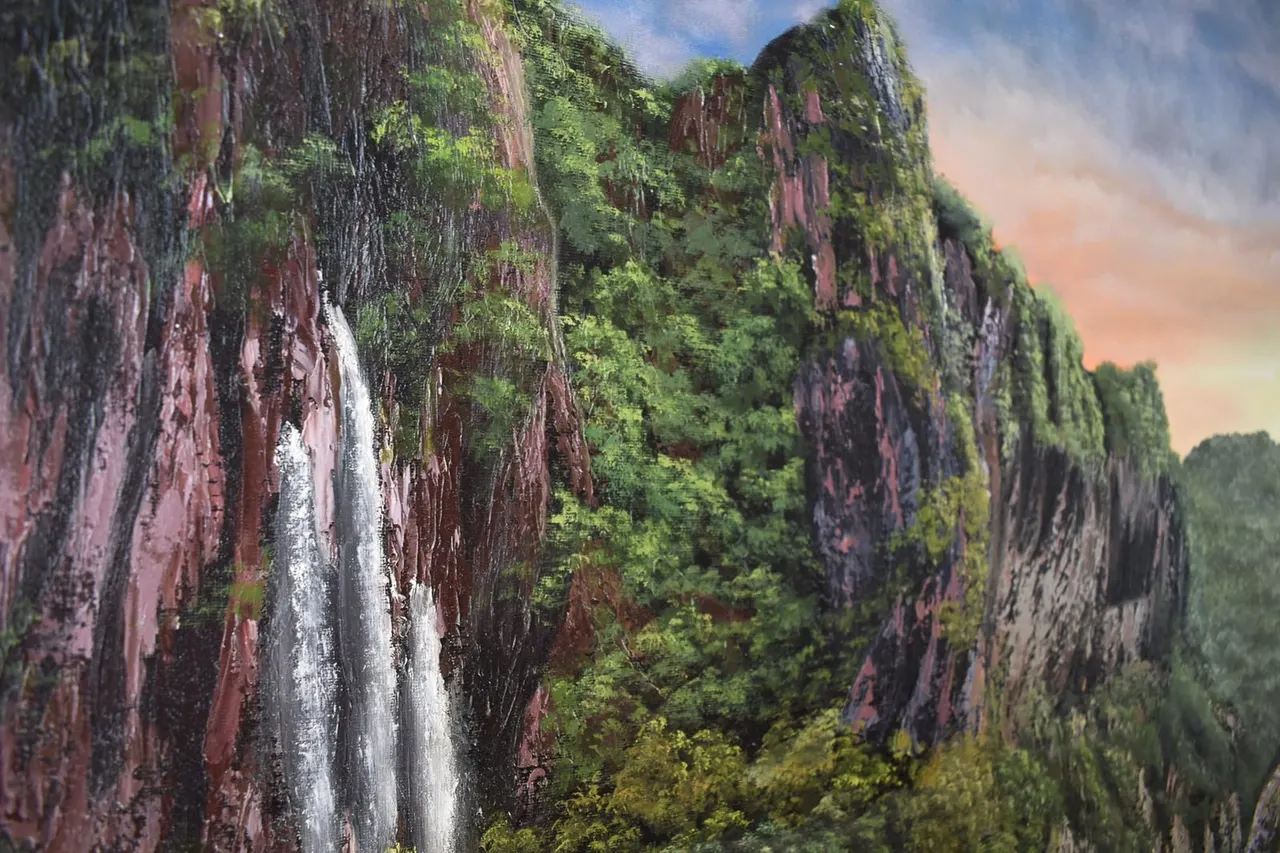 Waterfall cascading down moss-covered red rock cliffs surrounded by lush green vegetation and forest.