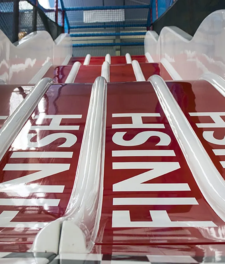Close-up of red and white inflatable slide lanes with handrails at an indoor play centre.
