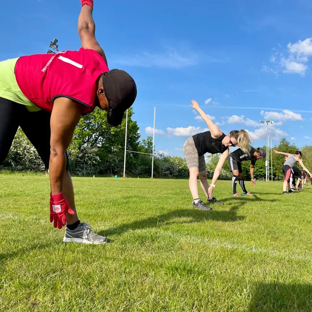 Young people exercising outdoors on a grass field with rugby posts visible in the background.