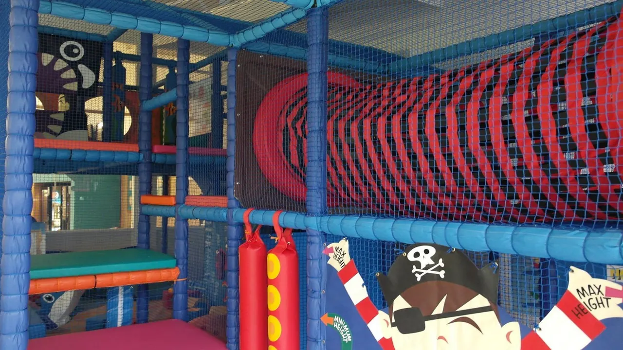 Interior of a colourful soft play structure with blue frames, red netting, and pirate-themed decorations including a skull and crossbones sign.