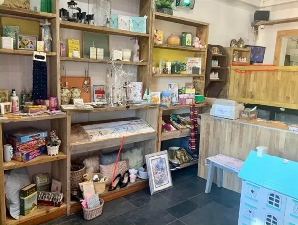Interior of a craft shop or gift store displaying handmade items, art supplies and merchandise on wooden shelves and counter.