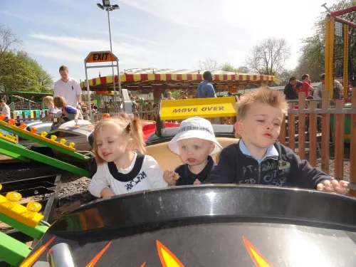 Three young children riding in the front car of a fairground ride at a leisure park.