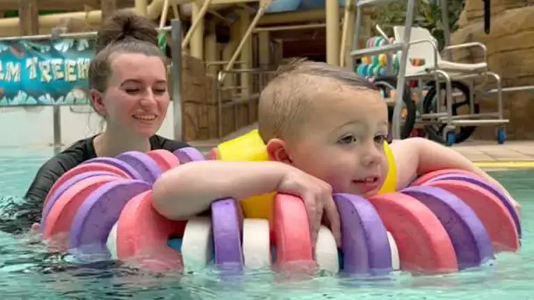 Young child and instructor in swimming pool with colourful inflatable aid during water lesson.