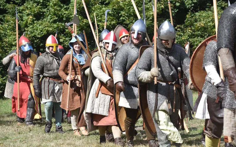 Line of people in period Viking and medieval armour and costumes holding spears and shields during a historical reenactment display.
