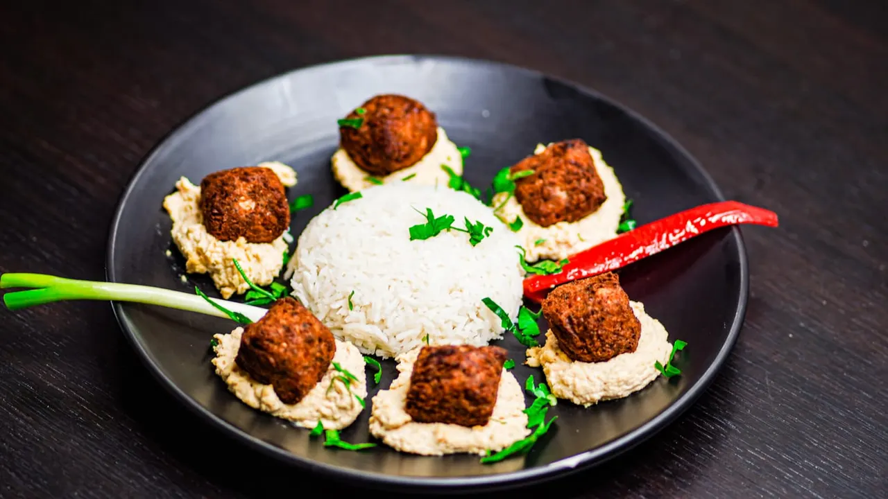 Plated Middle Eastern mezze dish with spiced meatballs on hummus, fresh herbs, and red chilli garnish.