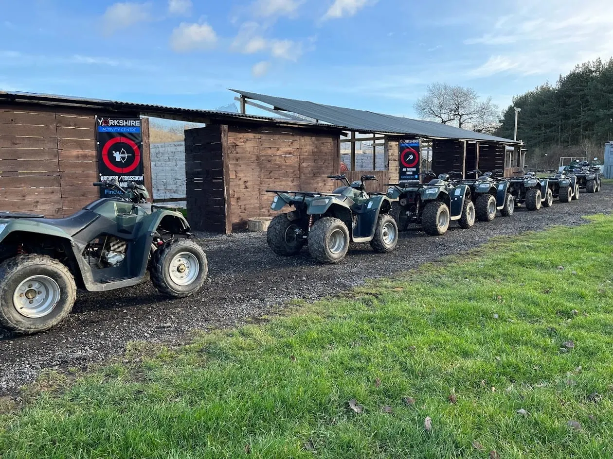 Row of quad bikes parked outside a wooden activity centre building with signage on a sunny day.