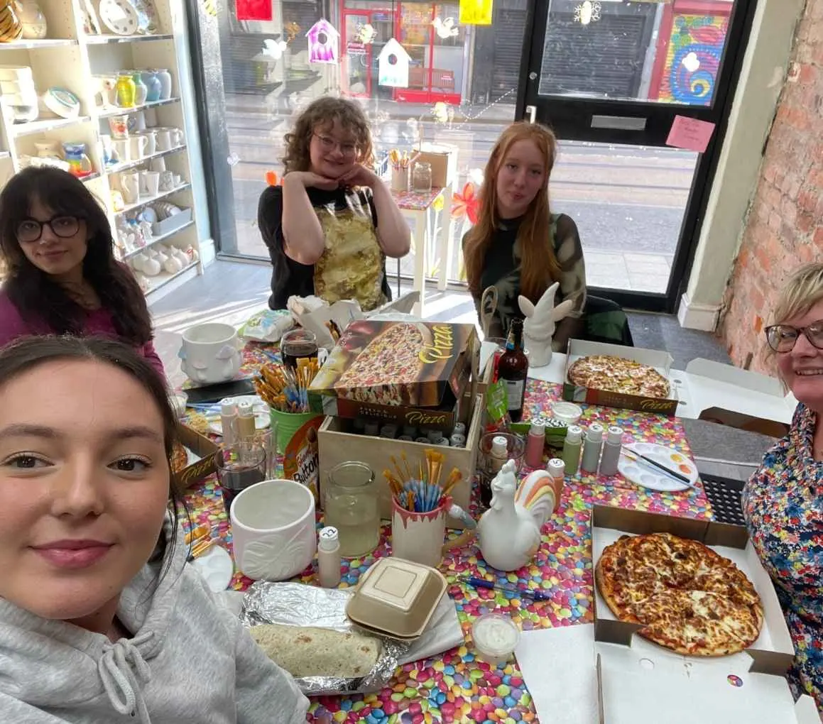 Small group of young people enjoying a pizza party at a ceramics studio workshop table.