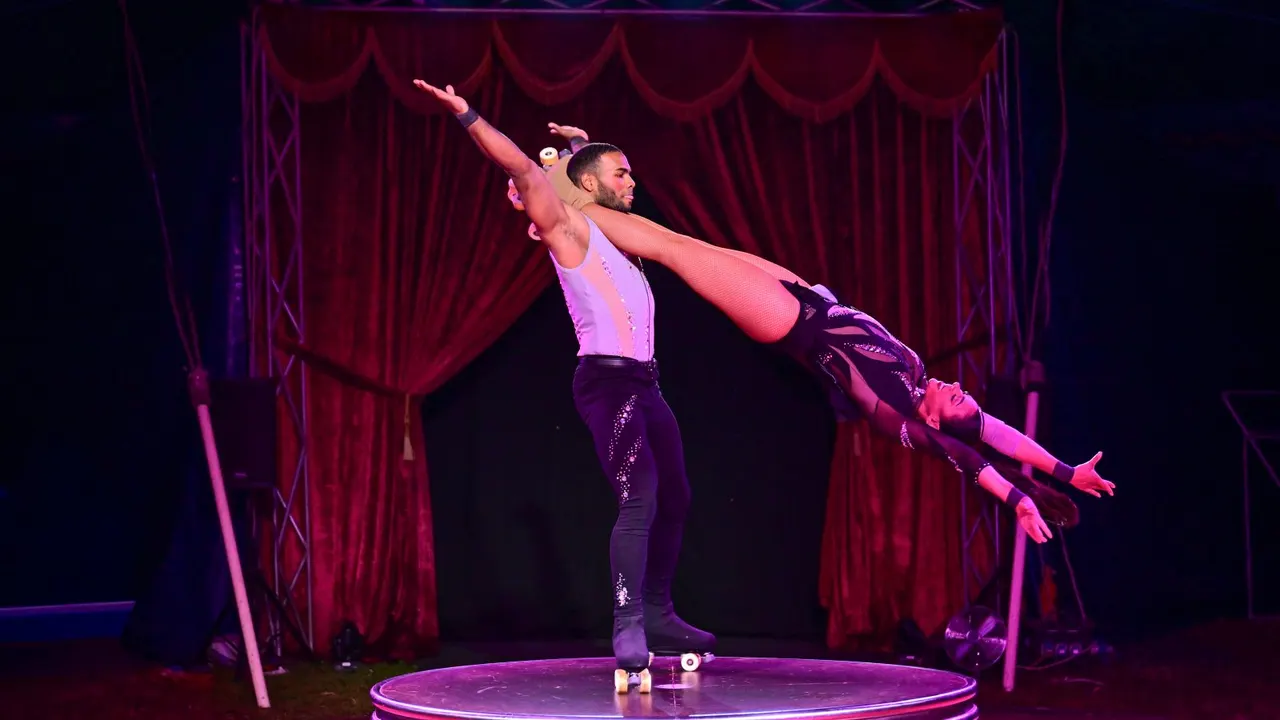 Acrobat performing an aerial balance pose on stage with red velvet curtains behind.