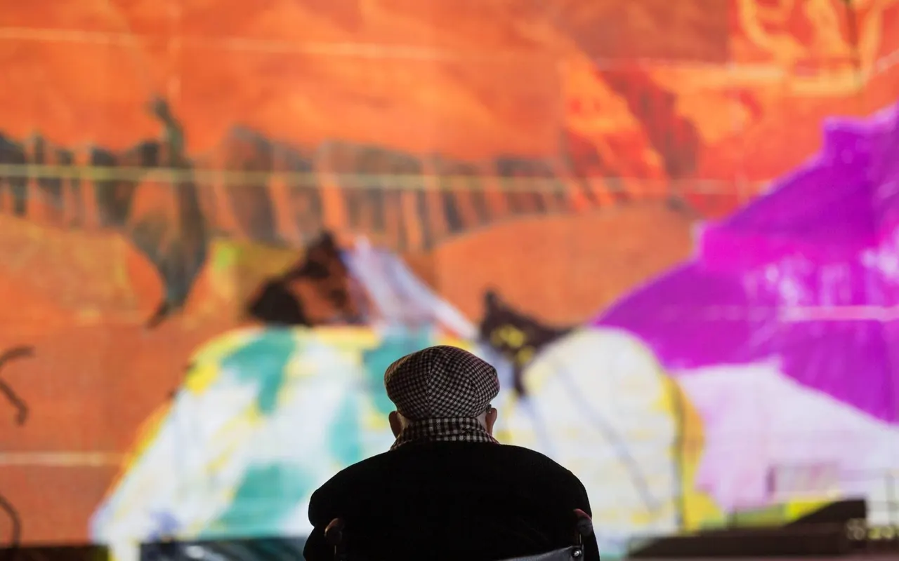 Person watching vibrant projected animation featuring stylised figures and colourful shapes on a large screen.