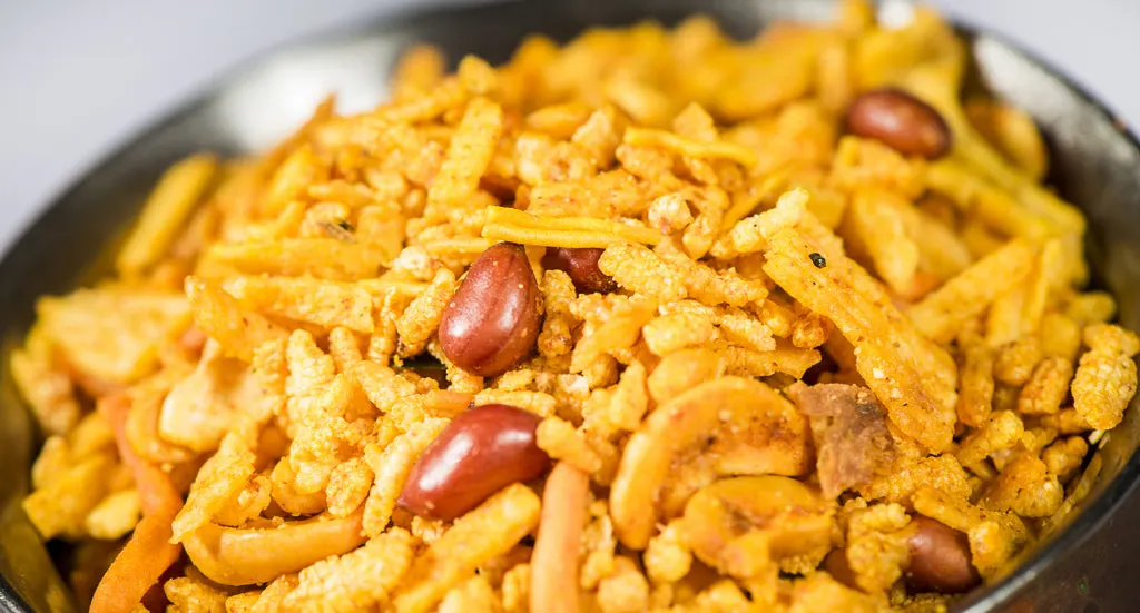Close-up of a bowl of spiced Indian snack mix with peanuts and cashews.