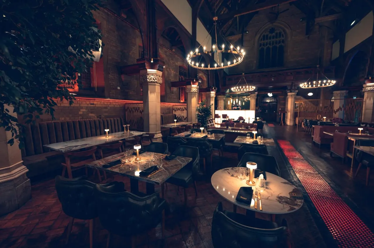 Elegant dining room in a converted church with vaulted ceilings, ornate chandeliers, and tables set for service.
