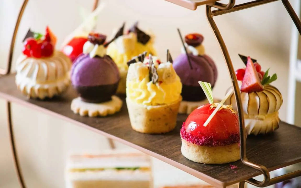Decorative petit fours and desserts with various toppings and glazes displayed on a dark tray.