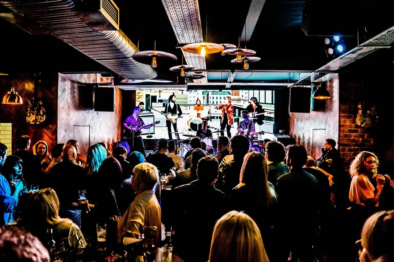A crowd of people watch a live band perform on stage in a modern venue with dramatic lighting and architectural features.