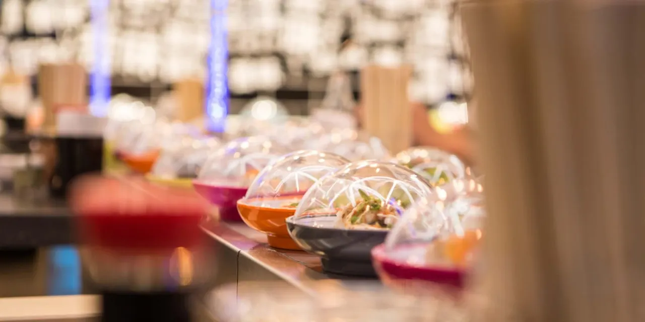 Covered bowls of Asian food on a counter with blue lighting and brick wall backdrop.
