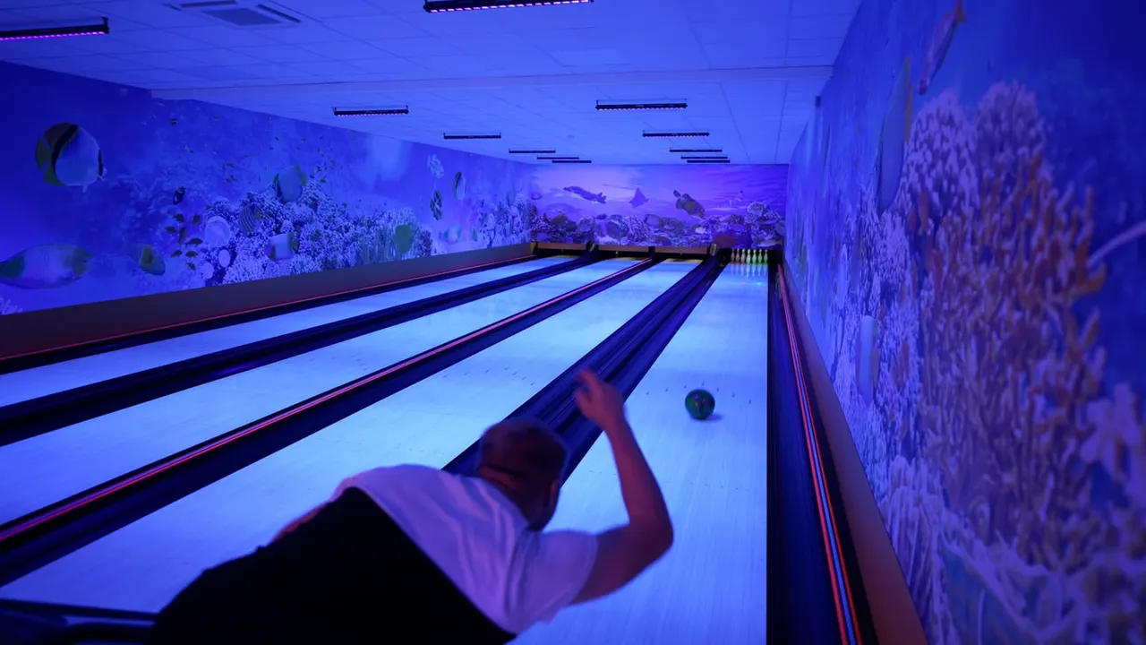 Person bowling in an indoor alley with glowing blue underwater-themed wall murals and neon lighting.