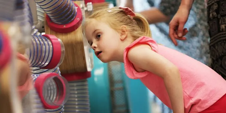 Young child examining large pink and blue coiled springs during a hands-on science activity.