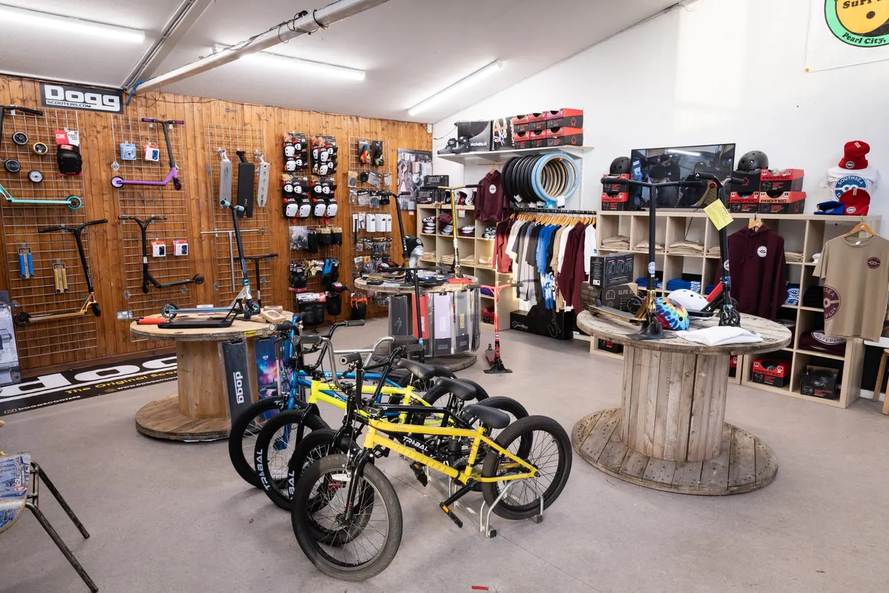 Interior of a skate shop displaying bicycles, scooters, protective gear, clothing and accessories on shelves and pegboards.