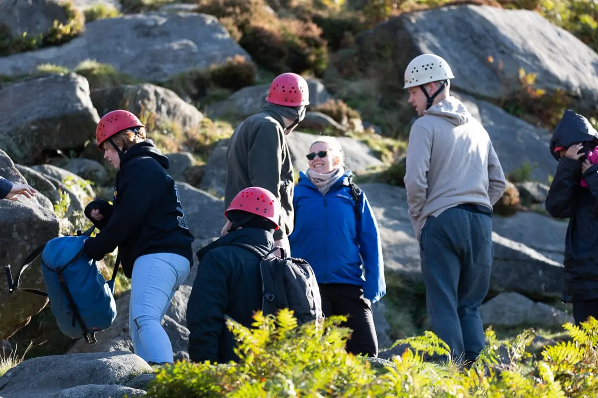 Group of visitors wearing climbing helmets gathered on a rocky outcrop during an outdoor activity session.