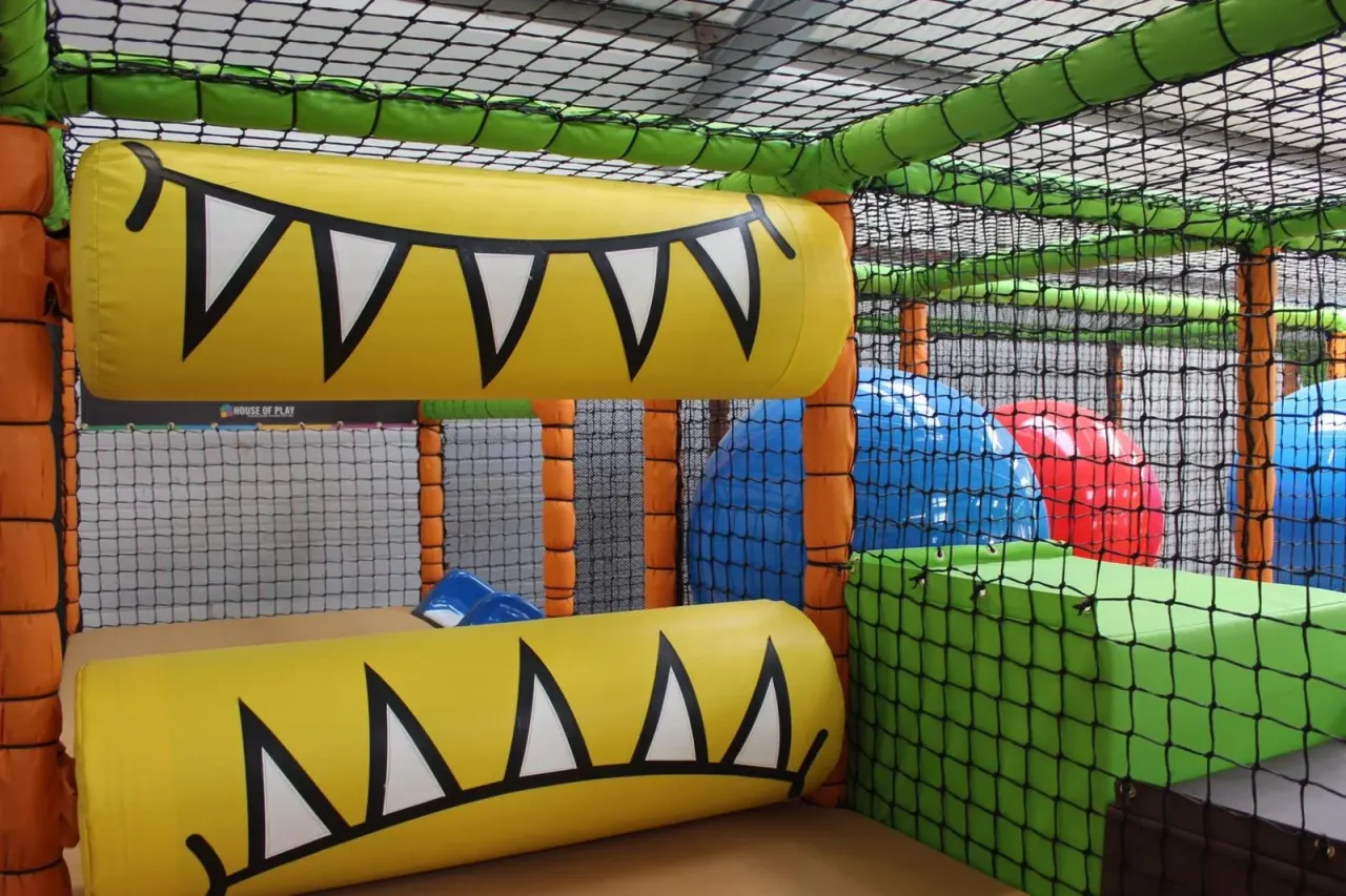 Interior of a soft play structure with yellow inflatable tunnels, coloured foam blocks and safety netting.